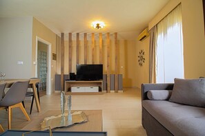 A living room with a flat-screen TV, a sofa, a dining table with chairs, and a decorative wall panel.