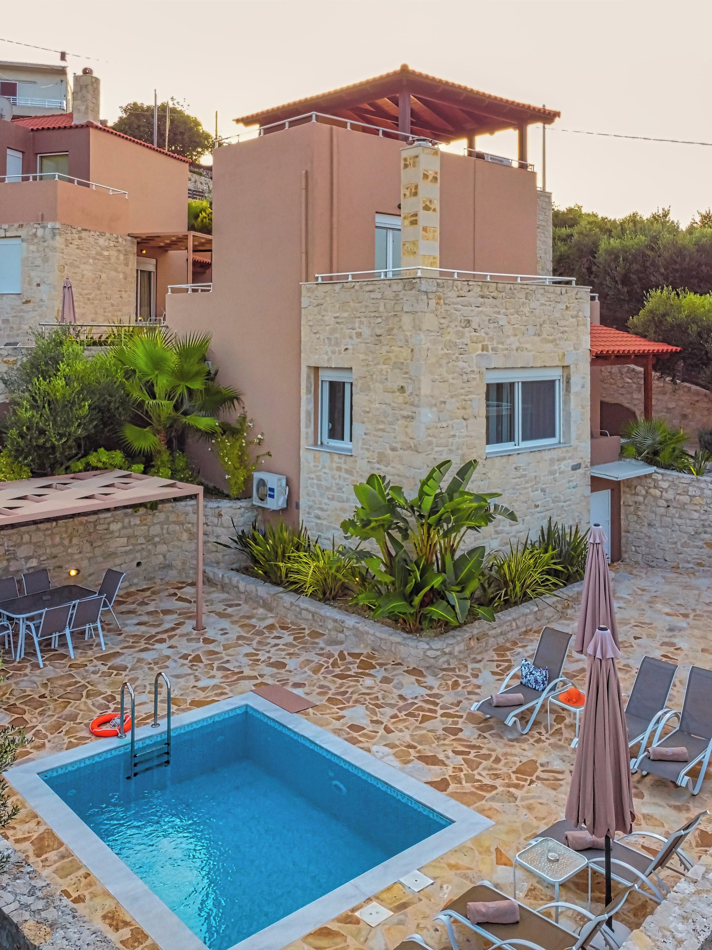 A swimming pool with lounge chairs and umbrellas, surrounded by stone walls and greenery.