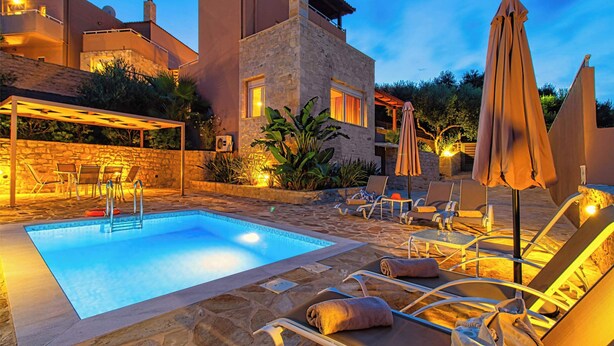 Un espace piscine avec des chaises longues et des parasols, des murs en pierre et un bâtiment en pierre doté de fenêtres.