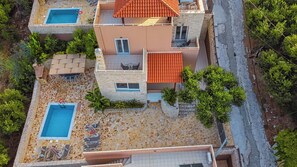 A two-story building with a swimming pool, outdoor seating, and a stone-tiled patio. - Rose Villa - Theo Villas With Sea View (Marathokefala)