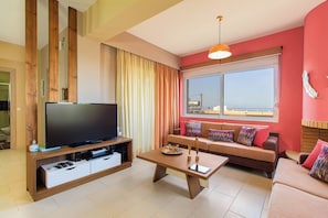 A living room with a flat-screen TV, wooden entertainment unit, sofa, coffee table, and a large window with curtains.