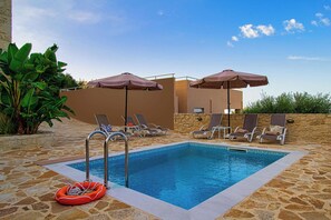 A swimming pool with lounge chairs and umbrellas, surrounded by stone tiles and greenery.