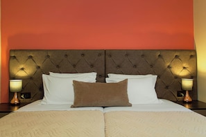 A double bed with a tufted headboard, two bedside lamps, and a brown accent pillow.
