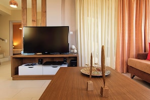 A modern living room with a flat-screen TV on a wooden stand, a dining table with a decorative centerpiece, and a sofa with a red cushion.