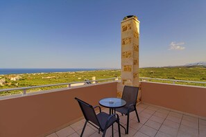 A balcony with a table and chairs, a stone pillar, and a view of a coastal landscape.
