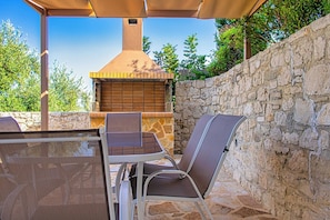 An outdoor patio with a stone wall, a grill, and a table with chairs.