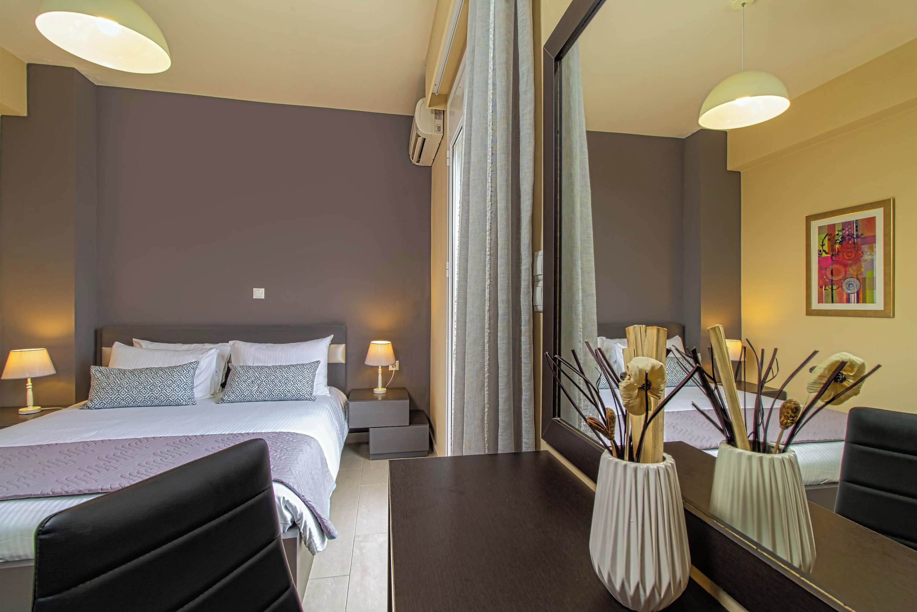 Ett hotellrum med en säng, sängbord, lampor, en spegel och dekorativa vaser.