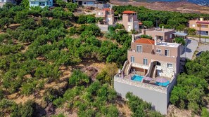 A modern villa with a pool, surrounded by dense greenery and a hilly landscape.