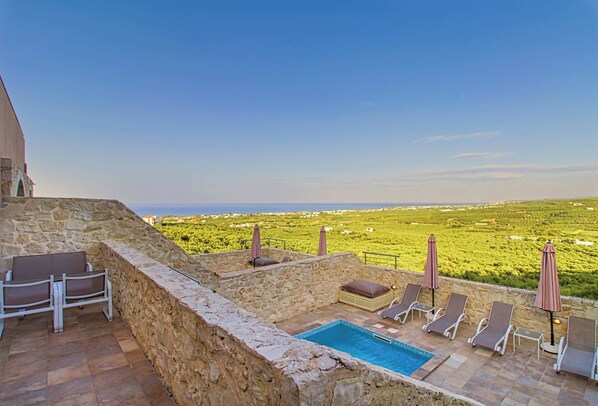 A stone-walled outdoor area with a pool, lounge chairs, and umbrellas.