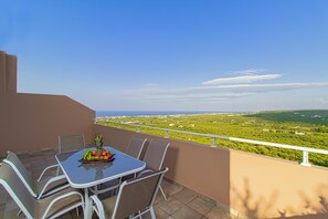 A balcony with a table set for dining, featuring a fruit bowl and chairs.
