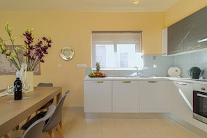 Een moderne keuken met witte kasten, een eettafel met stoelen, een fruitschaal en een vaas met bloemen.