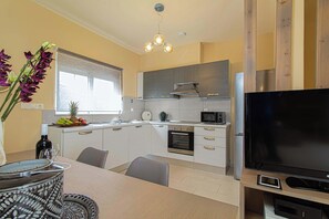 Een moderne keuken met witte kastjes, een ingebouwde oven, een magnetron en een grote flatscreen-televisie.