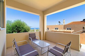 Een balkon met een glazen tafel en twee stoelen, met uitzicht op een schilderachtig zeegezicht en groen.