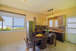 A modern kitchen with a dining area, large windows, and a view of the sea. - Lillium Villa - Theo Villas With Sea View (Marathokefala)