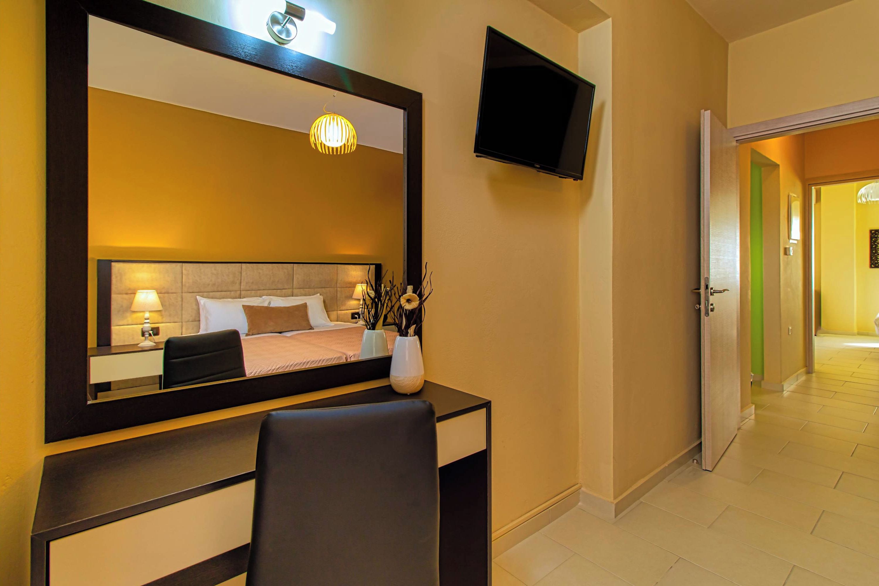 A hotel room with a bed, bedside table, lamp, TV, and a desk with a chair.