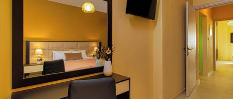 A hotel room with a bed, bedside table, lamp, TV, and a desk with a chair.