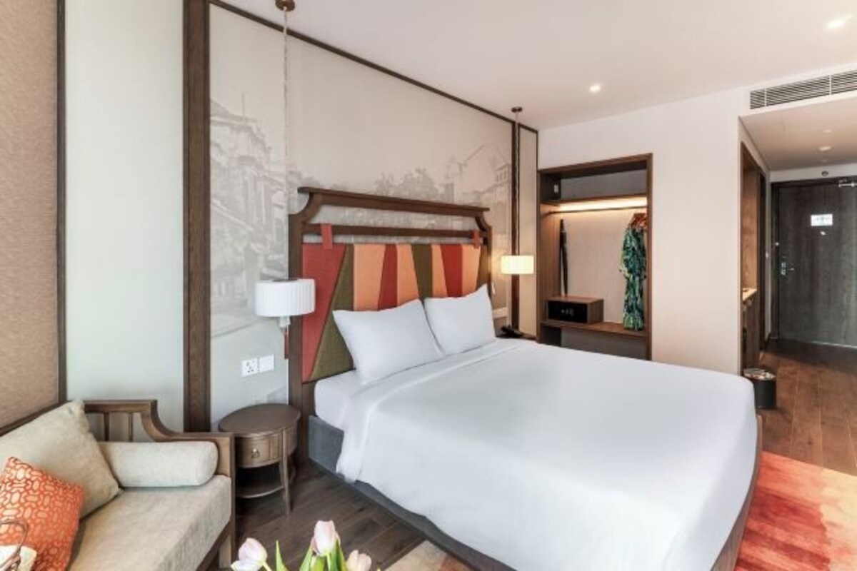 A modern hotel room with a large bed, a sofa, a nightstand, and a mirror.