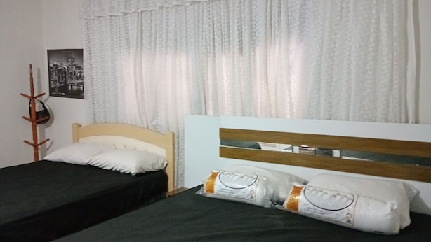 Una habitación con dos camas individuales, cabecero de madera, perchero y un cuadro en la pared.
