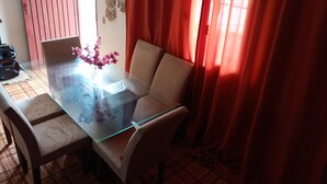 Un comedor con una mesa de vidrio, sillas color beige y un jarrón con flores rosadas.