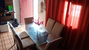 Un comedor con una mesa de vidrio y cuatro sillas, una mesita blanca y una cortina roja.