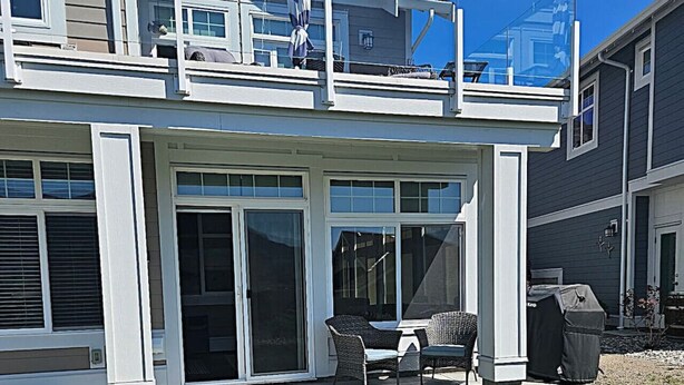 Et toetagers hus med en overdækket terrasse, en skydedør og et lille udendørs siddeområde med stole.