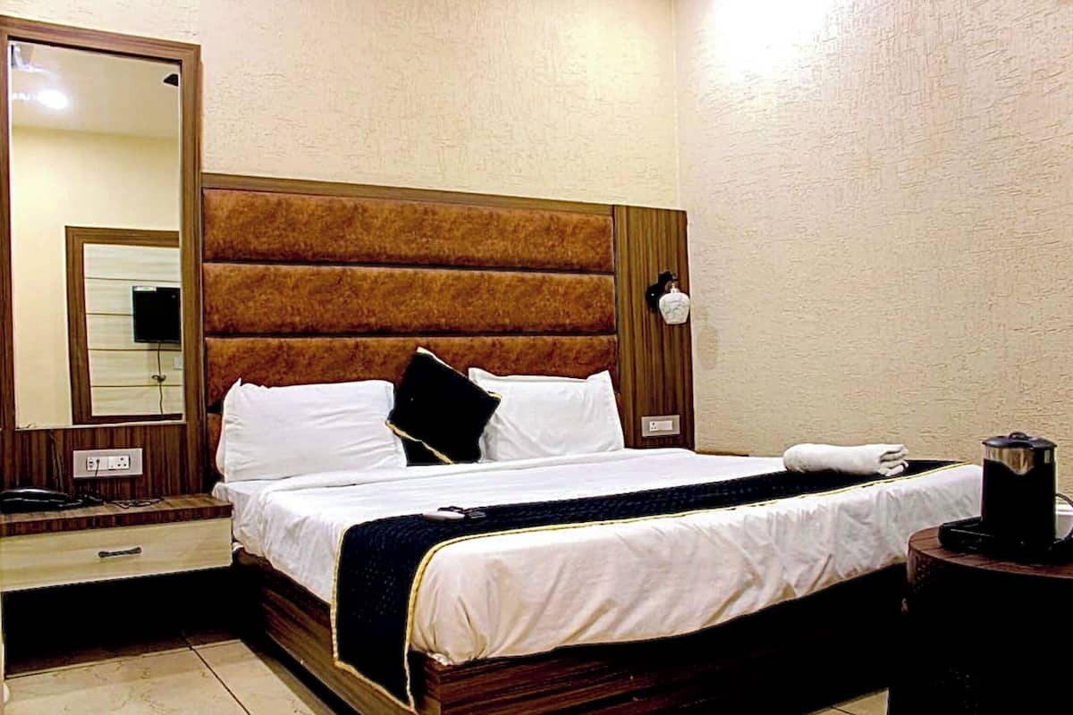Habitación de hotel con una cama grande, una mesita de noche con lámpara, un espejo y una cafetera.