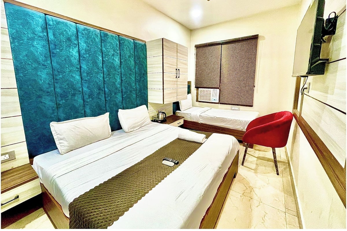 Una habitación de hotel con dos camas individuales, una silla roja, un ventilador de techo y una ventana con persianas.