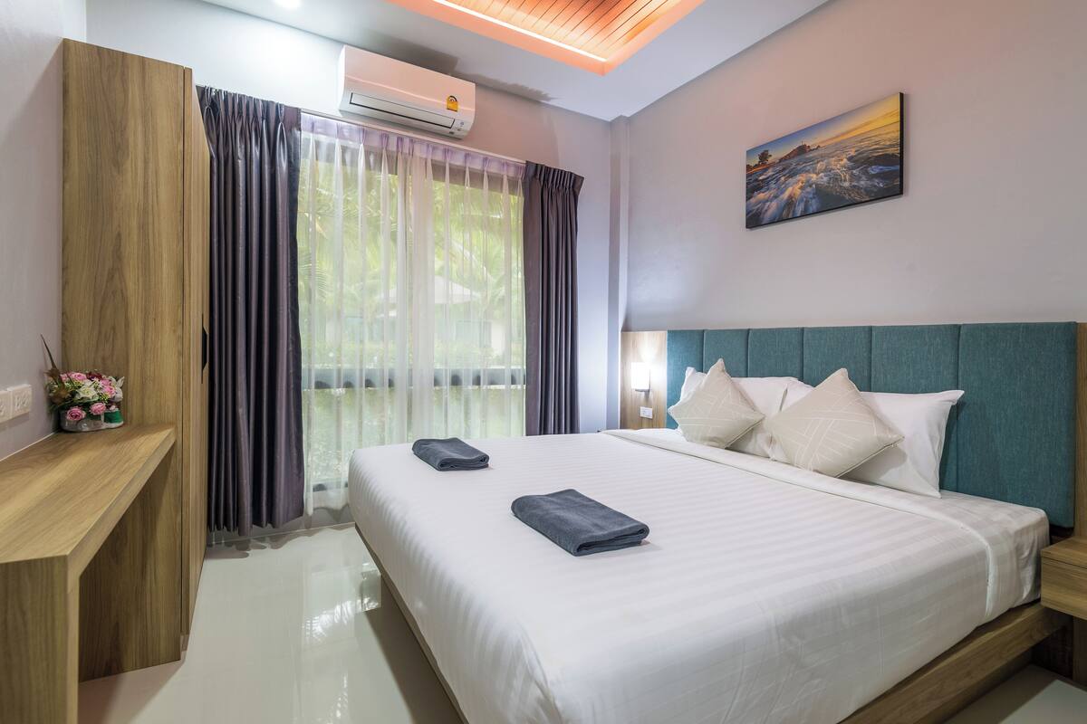 A hotel room with a large bed, a wooden desk, a nightstand, and a painting on the wall.