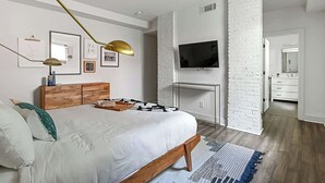 A modern bedroom with a bed, bedside table, lamp, TV, and a brick accent wall. - Le Venture (Atlanta)