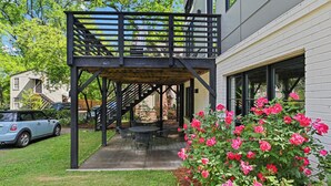 A covered patio with a table and chairs, a staircase, and a rose bush. - Le Venture (Atlanta)
