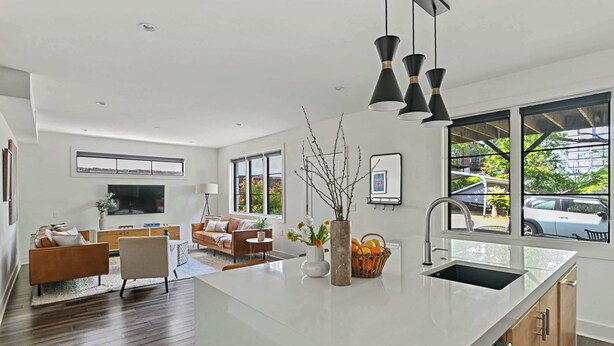 A modern kitchen with a large island, a dining area with a sofa and chairs, and a living room with a TV and decorative items. - Le Venture (Atlanta)