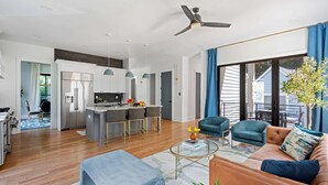 A modern living room with a sofa, coffee table, and a dining area with chairs and a kitchen in the background.