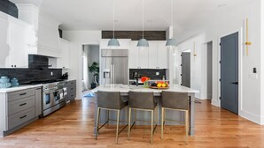 A modern kitchen with a central island, grey cabinetry, stainless steel appliances, and pendant lighting.