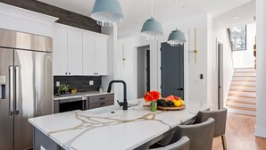 A modern kitchen with white cabinets, a marble island, and pendant lighting.