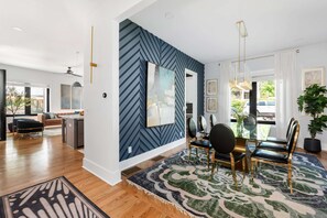 Un salon moderne avec un coin repas, comprenant un mur orné d’un motif en chevrons, un grand miroir et une table à manger avec des chaises.