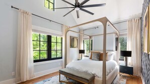A four-poster bed with a bench, large windows, and a ceiling fan in a bedroom.
