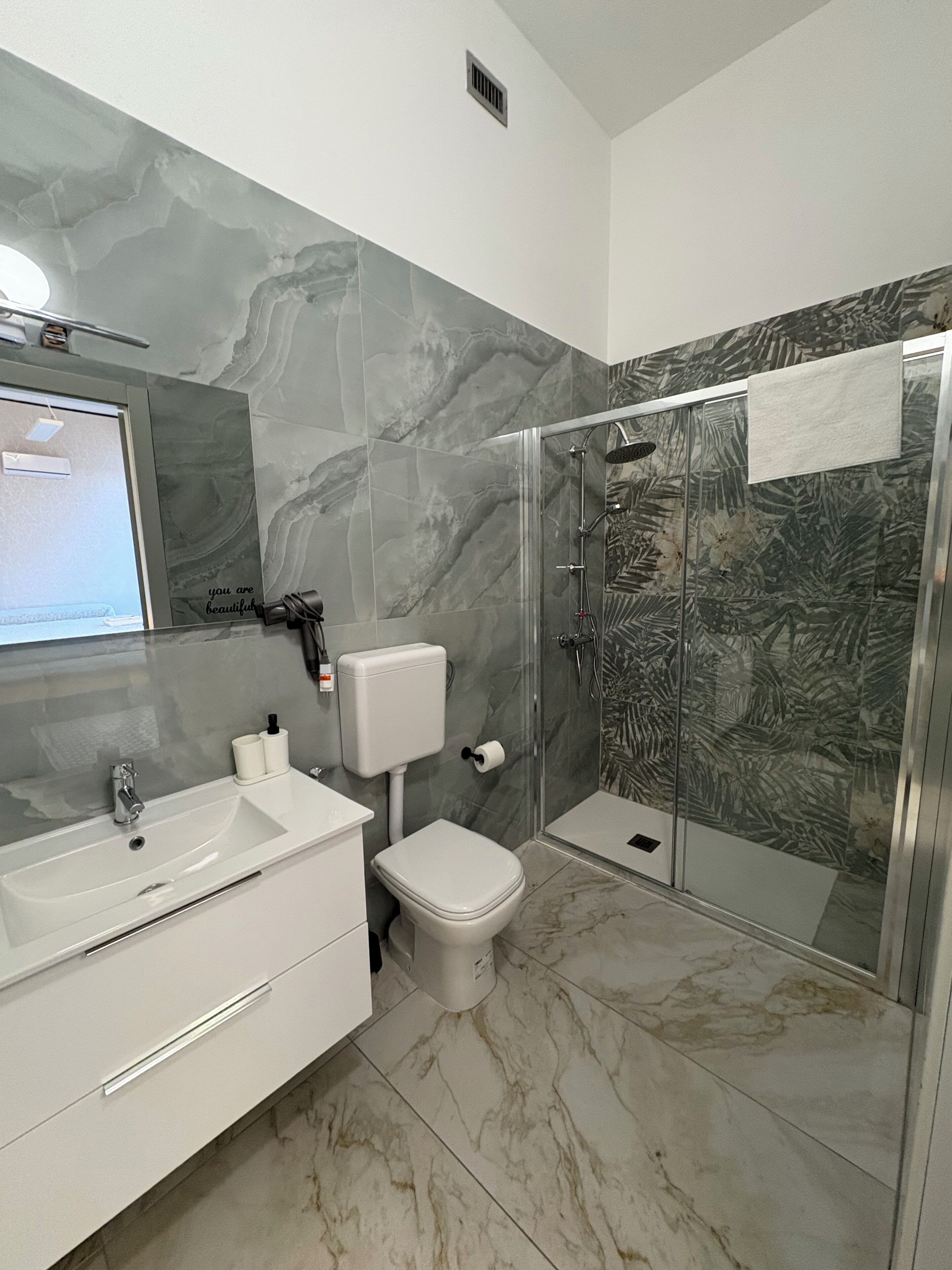 A bathroom with a marble floor, a white sink, a toilet, and a shower with a glass door.