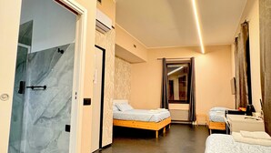 Une chambre d’hôtel avec une douche en verre, deux lits, un petit bureau et un miroir.