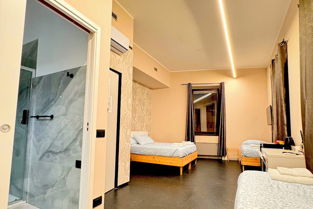 A hotel room with a glass-enclosed shower, two beds, a small desk, and a mirror.