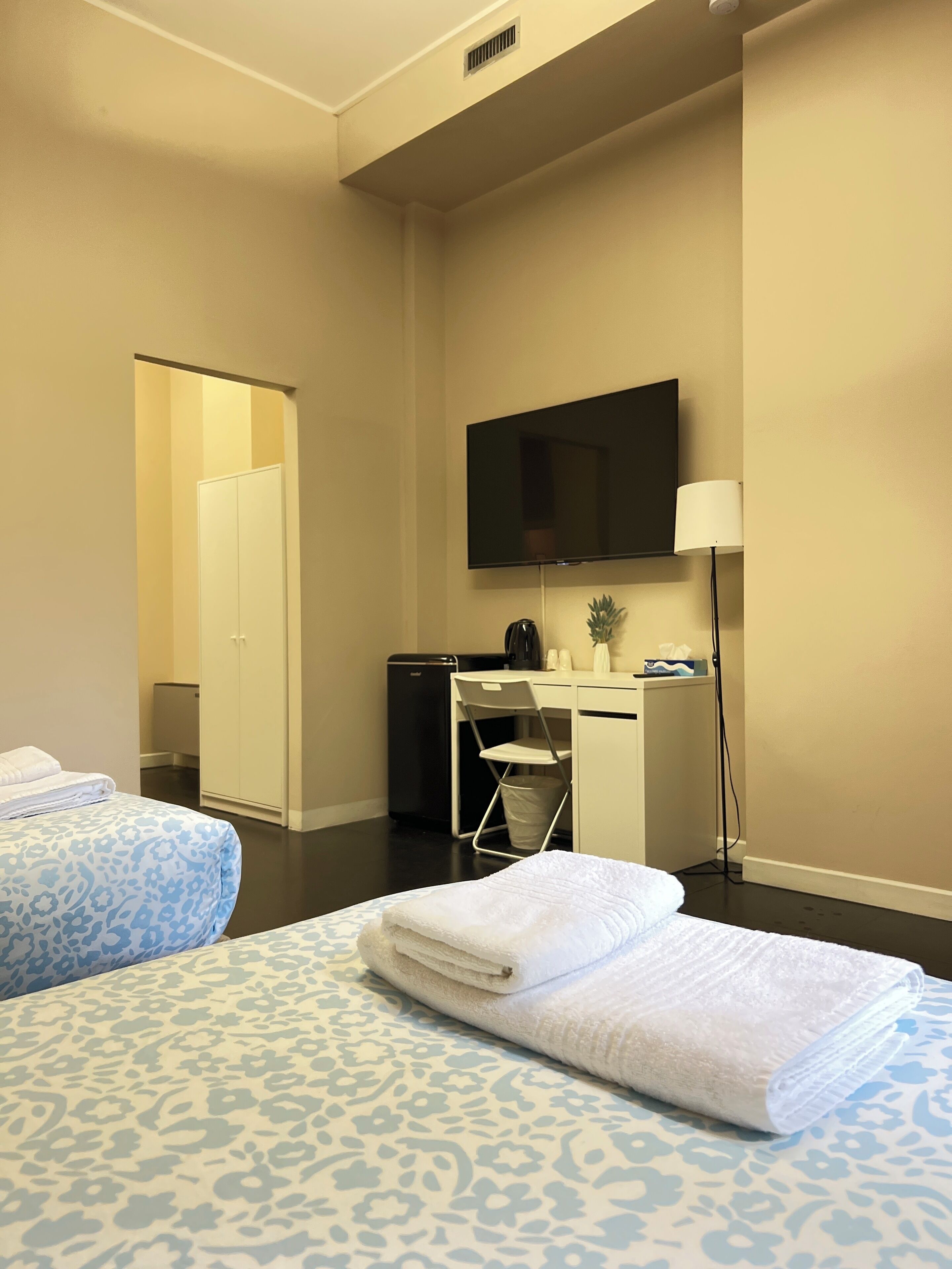 A hotel room with two beds, a desk, a chair, a television, and a lamp.