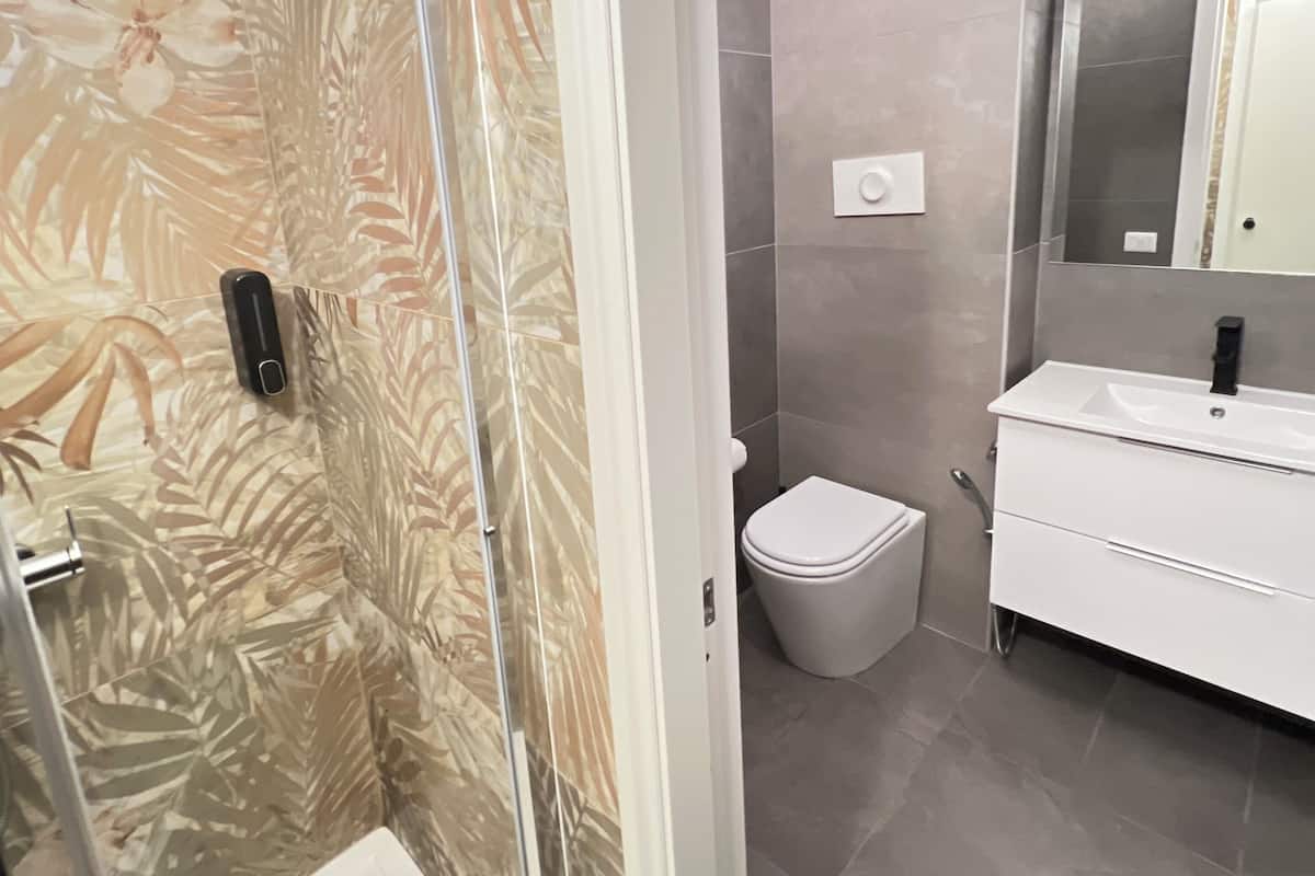 A modern bathroom with a glass shower enclosure, a toilet, and a vanity with a mirror.