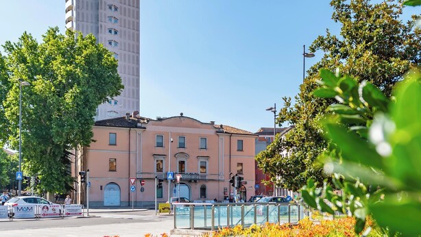 Un bâtiment à la façade rose, un grand arbre au premier plan et un ciel bleu dégagé.