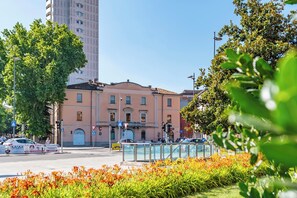 Un bâtiment à la façade rose, un grand arbre au premier plan et un ciel bleu dégagé.