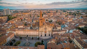 Un paysage urbain historique, dominé par une église remarquable avec un haut clocher, entourée de bâtiments très rapprochés et d’une place centrale.