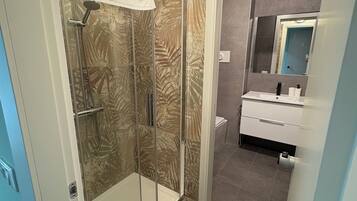 A bathroom with a glass shower enclosure, a white sink, and a mirror.