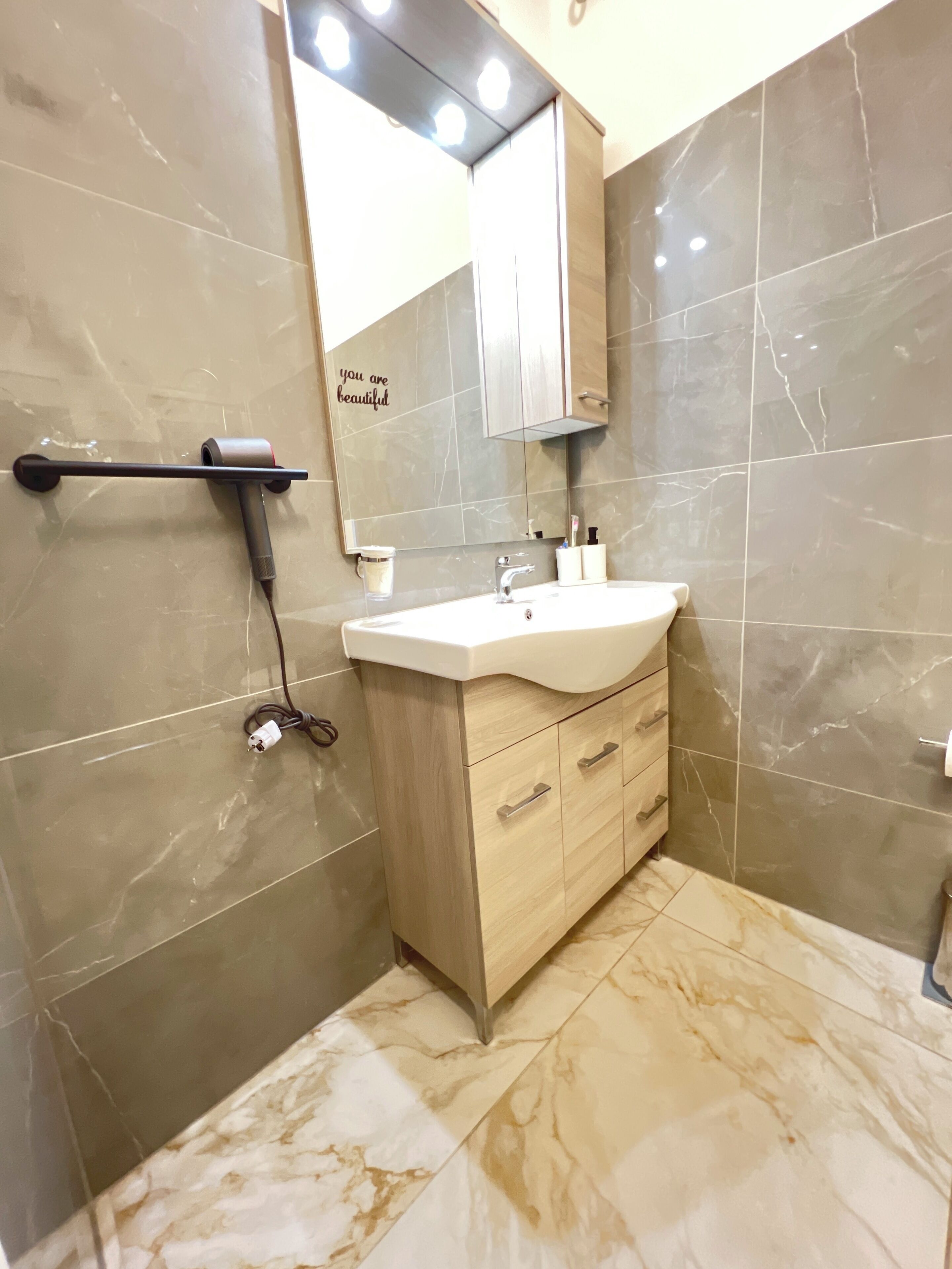 A modern bathroom with a marble floor, a vanity with a sink, a mirror, and a towel rack.
