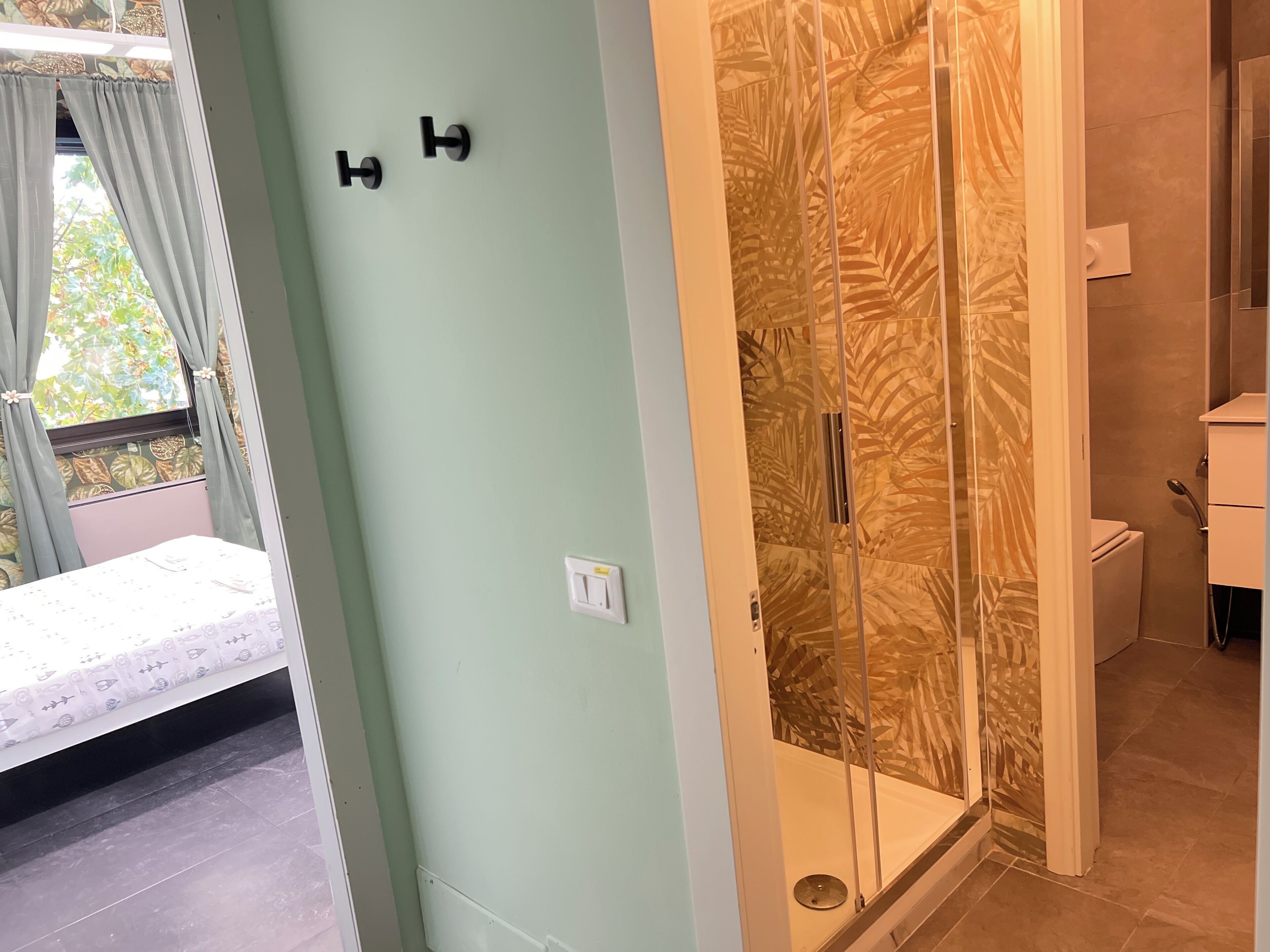 A room with a bed, a shower with a palm leaf pattern, and a toilet.