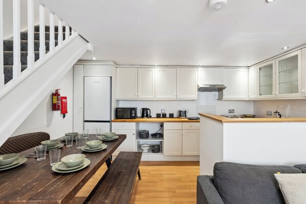 Une cuisine moderne avec des meubles blancs, un plan de travail en bois et un coin repas comprenant une table en bois dressée pour quatre personnes.