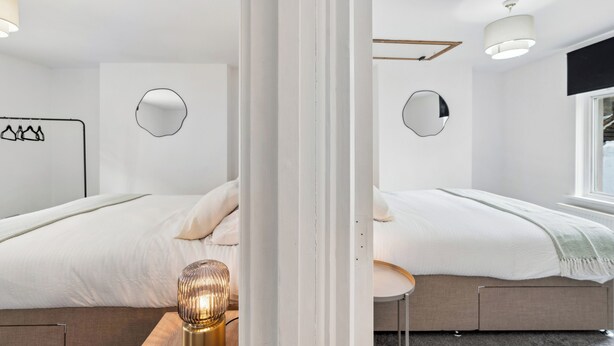 A modern hotel room with two beds, a small round table, and a wall-mounted TV. - Group & Contractor-Friendly 4Bed House (Brighton and Hove)
