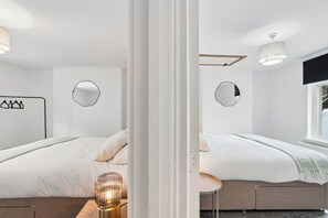 Une chambre d’hôtel moderne avec deux lits, une petite table ronde et un téléviseur fixé au mur.